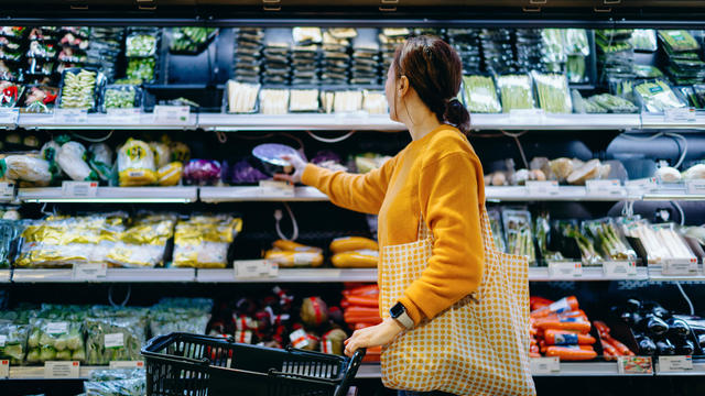 Young Asian woman with shopping cart, carrying a reusable shopping bag, shopping for fresh organic fruits and vegetables in supermarket. Environmentally friendly concept. Zero waste and plastic free. Eco friendly shopping. Sustainable living lifestyle 