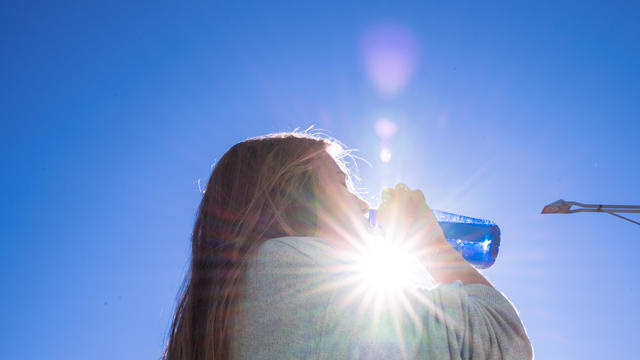 Blonde woman drinking water outside while being illuminated by a ray of sunlight. 