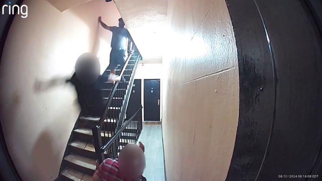 A still from Ring camera video footage shows a man falling down an apartment staircase after being kicked by another man standing on the stairs. 
